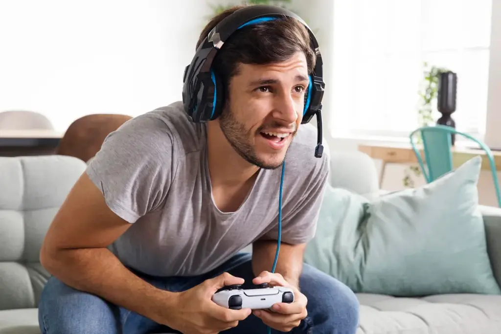 Homem jogando videogame no PlayStation com controle e headset gamer, concentrado durante partida.