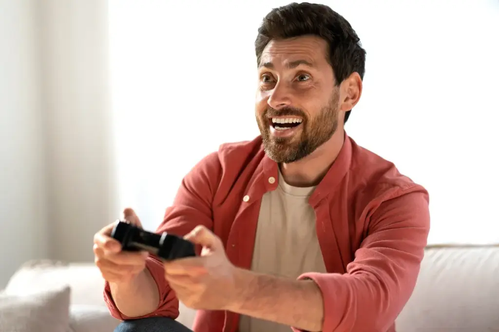 Homem sorrindo e empolgado enquanto joga FIFA no PlayStation usando controle de videogame.