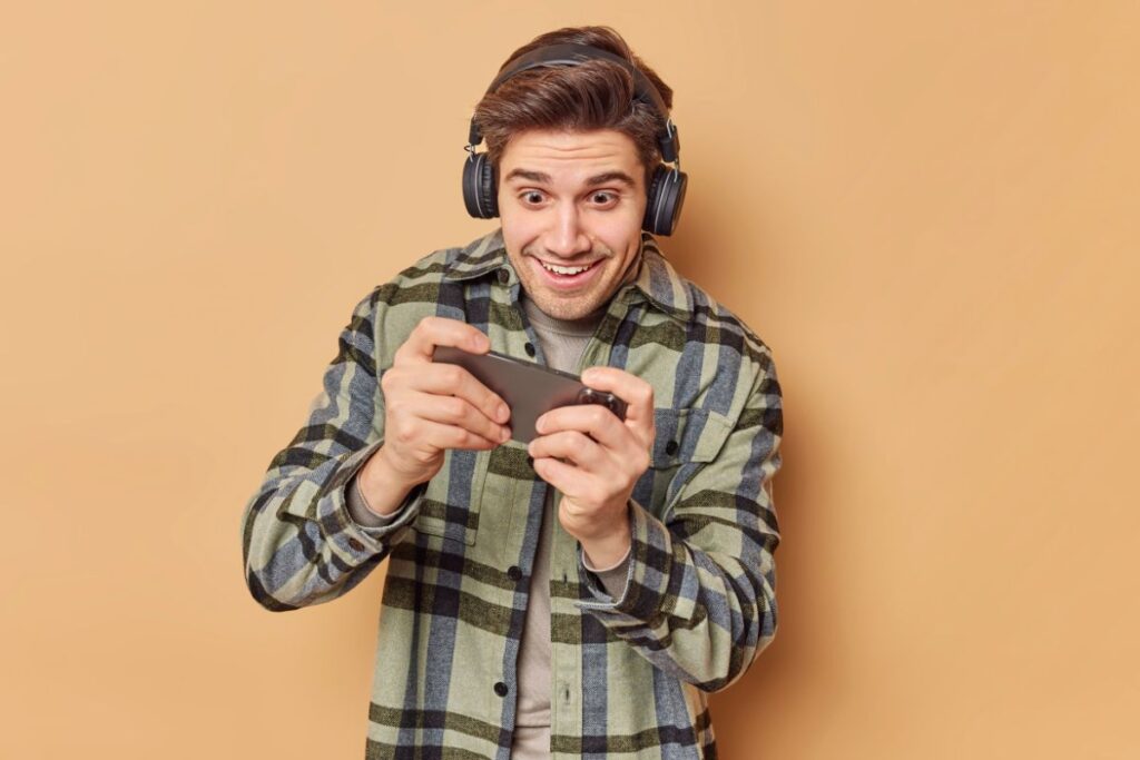 Homem sorridente usando o celular com fones de ouvido em fundo laranja, demonstrando entusiasmo
