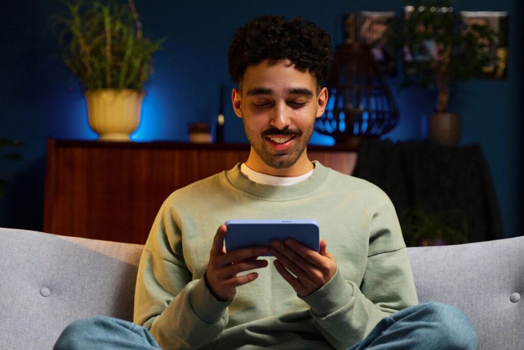 Homem sentado no sofá usando um tablet em casa à noite, em ambiente moderno e aconchegante