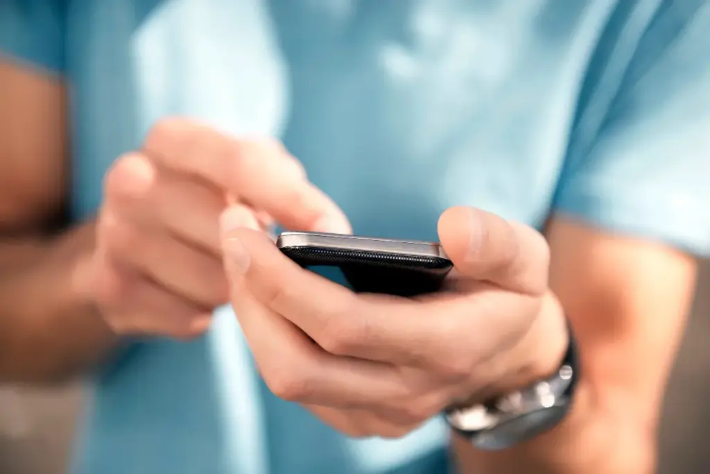 Close nas mãos de uma pessoa segurando um smartphone enquanto toca na tela com o dedo indicador.