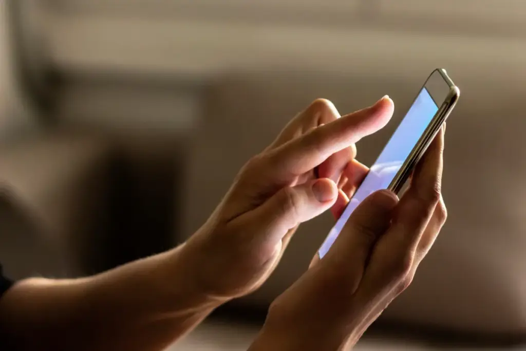 Close nas mãos de uma pessoa segurando um smartphone enquanto toca na tela com o dedo indicador.