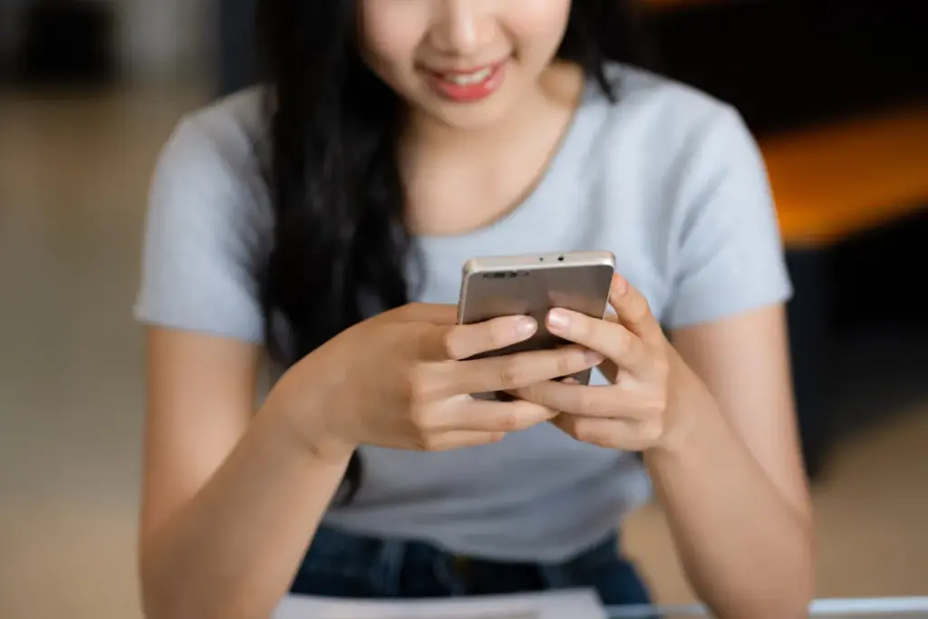 Mulher segurando um smartphone com as duas mãos enquanto digita na tela do aparelho.