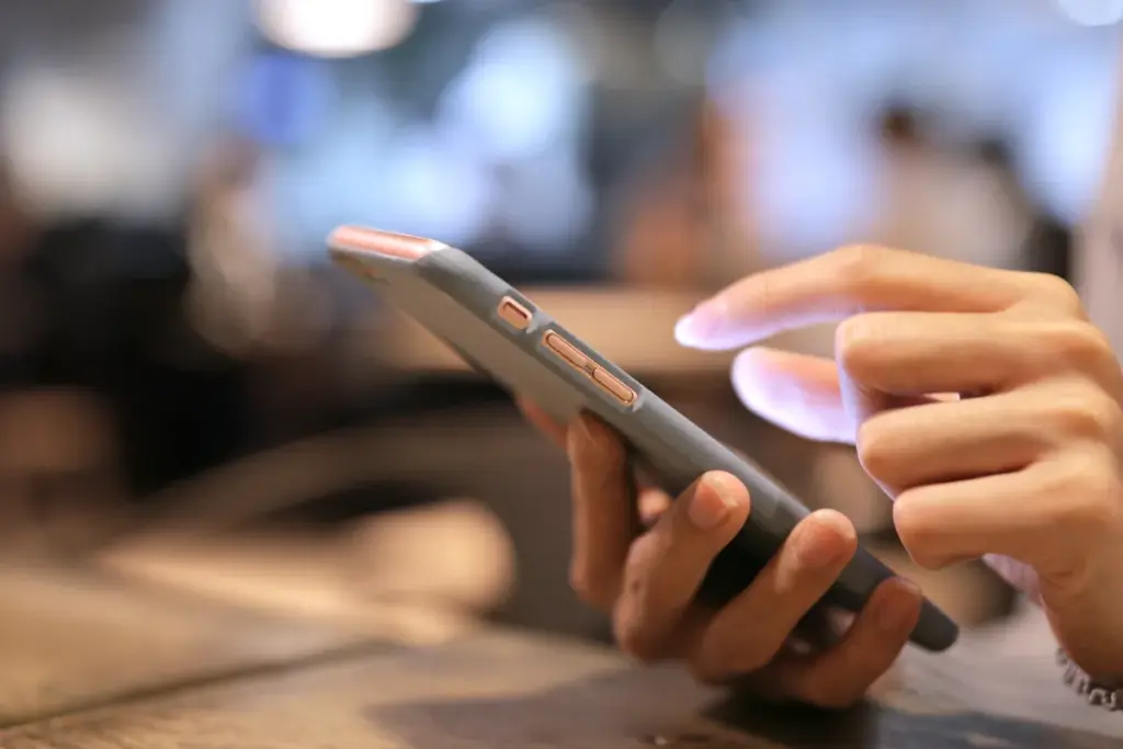 Close de uma mão segurando um smartphone enquanto o dedo indicador toca na tela do aparelho.