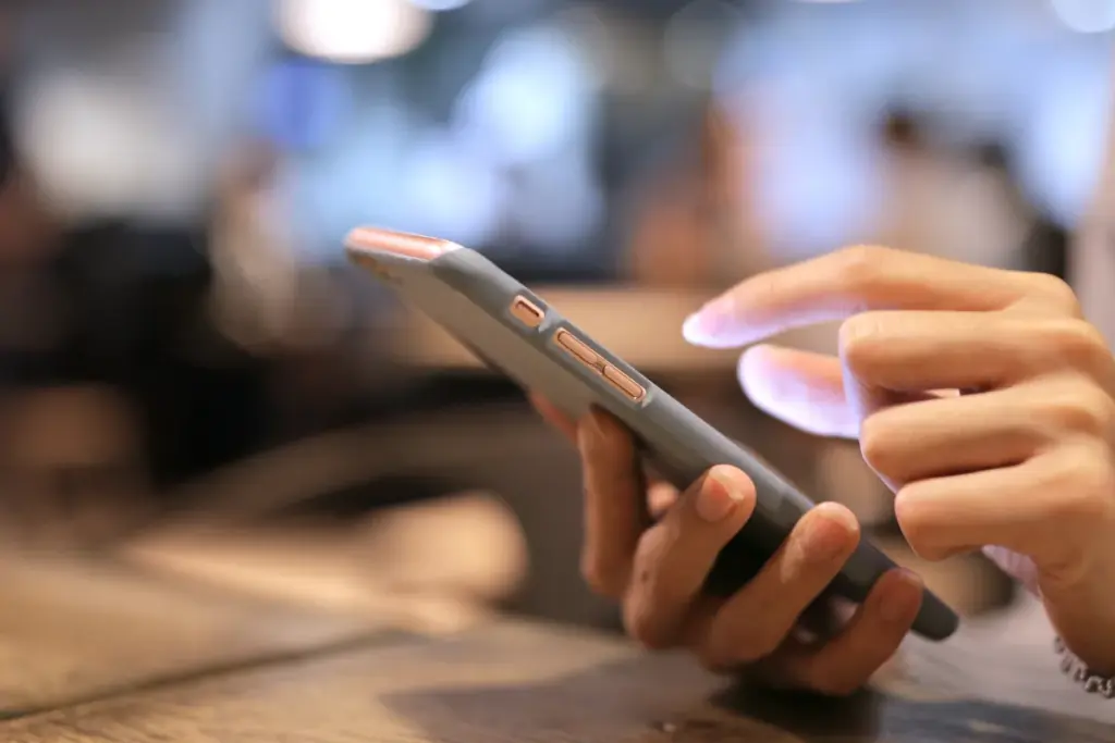 Close de uma mão segurando um smartphone enquanto o dedo da outra mão toca na tela do aparelho.