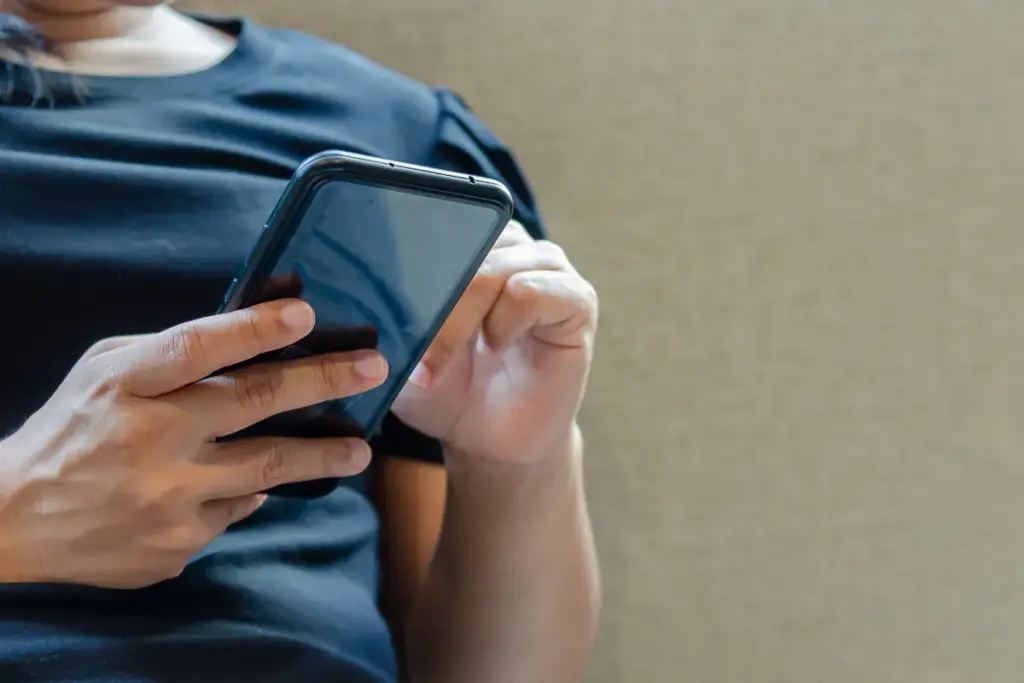 Pessoa segurando um smartphone preto enquanto toca na tela com o dedo indicador.