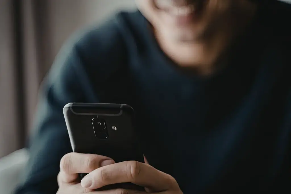 Close de uma pessoa segurando um smartphone preto enquanto observa a tela do aparelho.