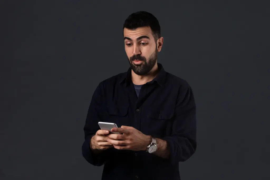 Homem olhando para o smartphone com expressão de surpresa enquanto segura o aparelho com as duas mãos.