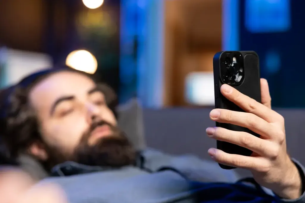 Homem deitado no sofá usando o celular em ambiente noturno com iluminação suave