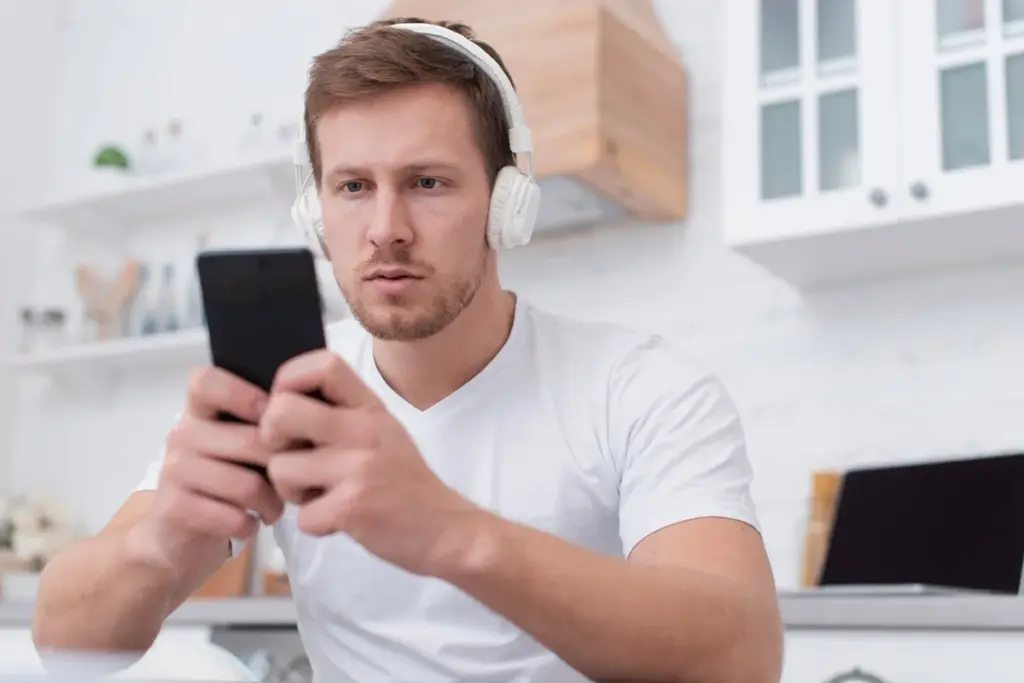 Homem com fones de ouvido usando o celular concentrado em ambiente doméstico