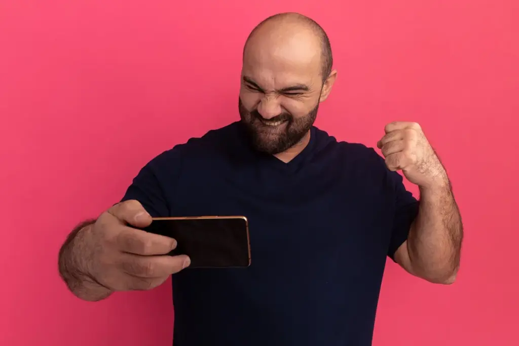 Homem comemorando enquanto olha para o celular em fundo rosa