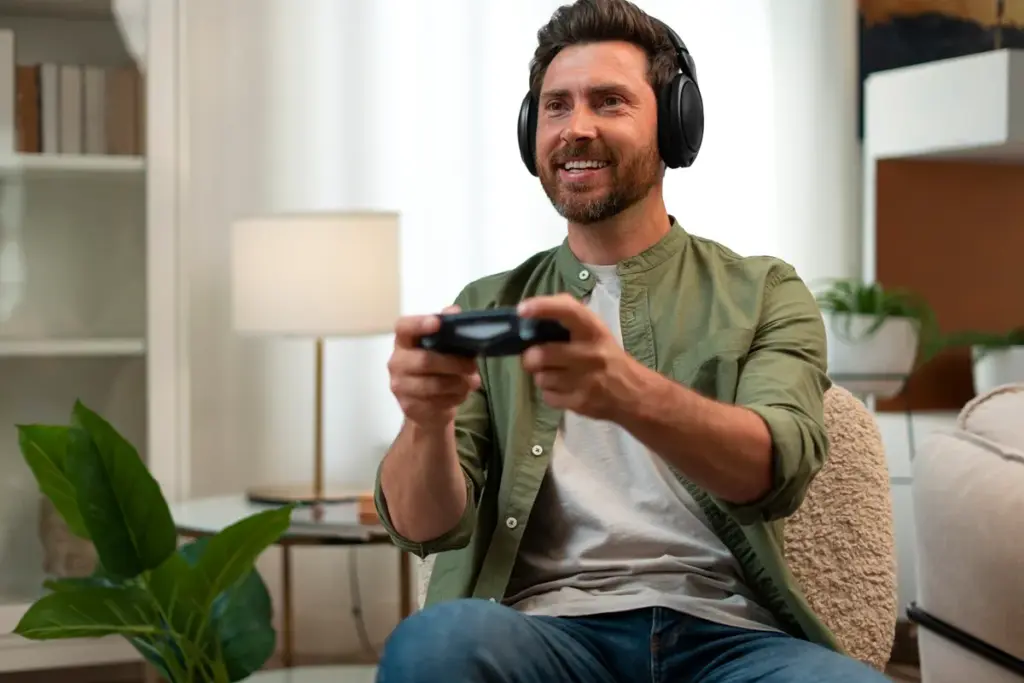 Homem sentado no sofá jogando videogame com controle nas mãos e usando fone de ouvido.