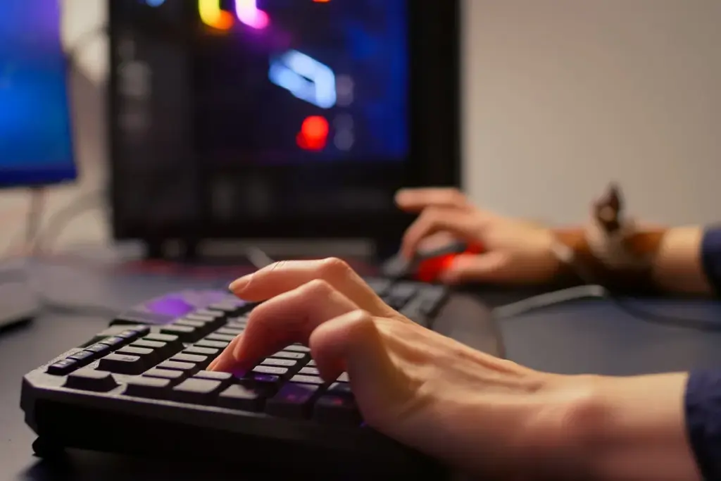 Mãos digitando em teclado mecânico gamer com iluminação RGB, em setup de computador para jogos