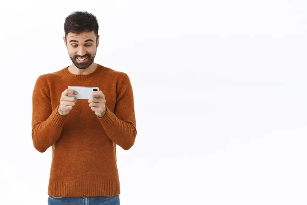 Homem sorrindo enquanto usa celular após comprar moedas em jogo online.