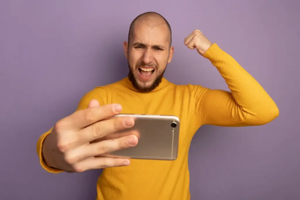 Homem careca comemorando vitória no celular com punho cerrado e expressão de alegria