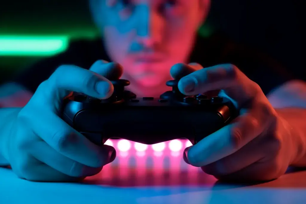 Pessoa segurando controle de videogame com luzes neon, jogando em ambiente escuro e imersivo.