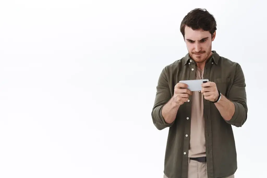 Homem segurando celular e jogando no smartphone com expressão de concentração.