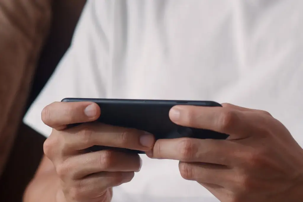 Mãos de uma pessoa segurando smartphone na horizontal enquanto joga no celular