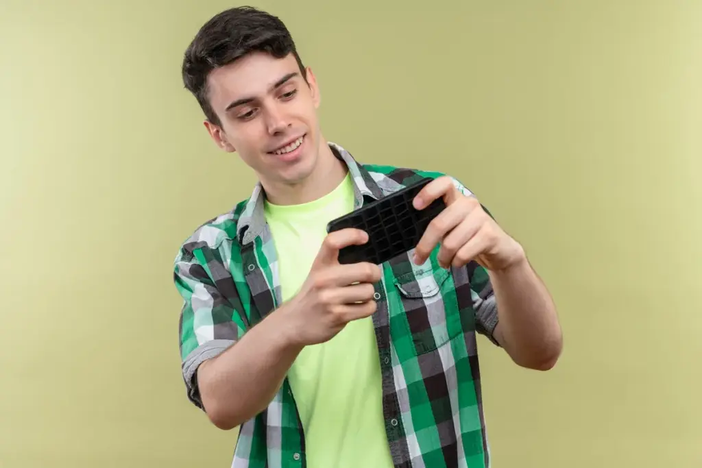 Homem jovem segurando celular na horizontal enquanto joga, vestindo camisa xadrez verde e camiseta verde clara, em fundo verde