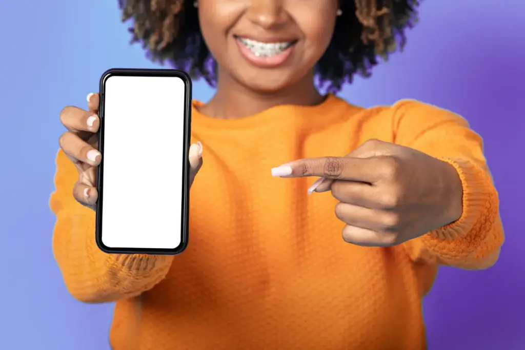 Mulher segurando um smartphone com a tela em branco enquanto aponta para o aparelho em fundo colorido.