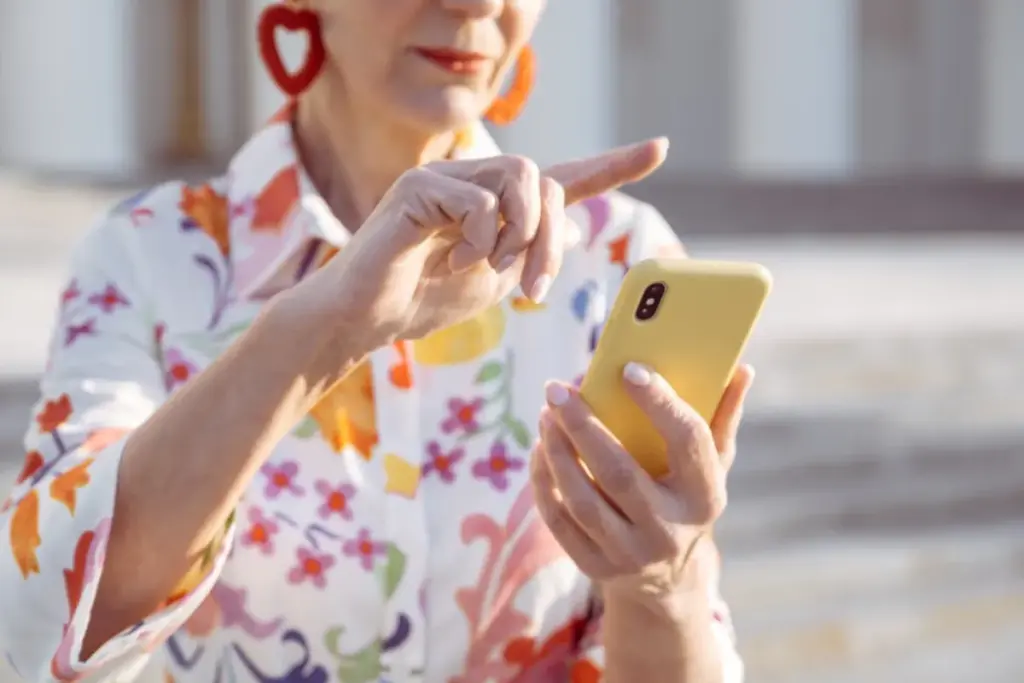 Mulher segurando um smartphone amarelo enquanto toca na tela do celular.