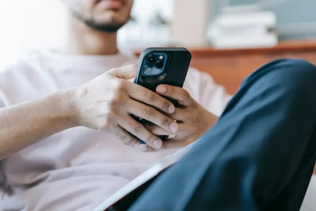 Homem sentado segurando um smartphone enquanto usa o celular com as duas mãos.