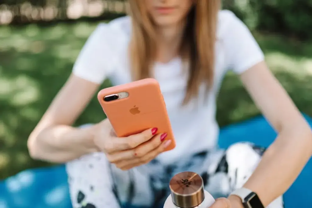 Mulher sentada ao ar livre segurando um smartphone com capa laranja enquanto olha para a tela.