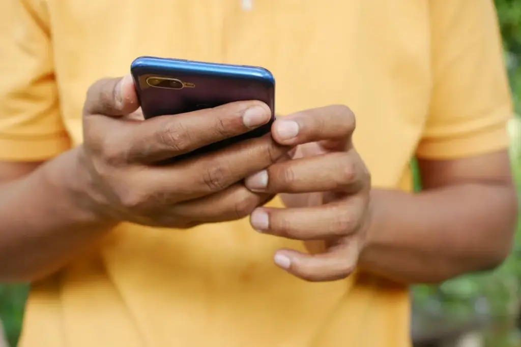 Pessoa segurando um smartphone azul com as duas mãos enquanto usa o celular.