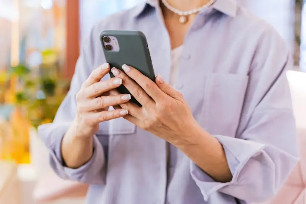 Pessoa segurando um smartphone com capa verde enquanto usa o celular com as duas mãos.