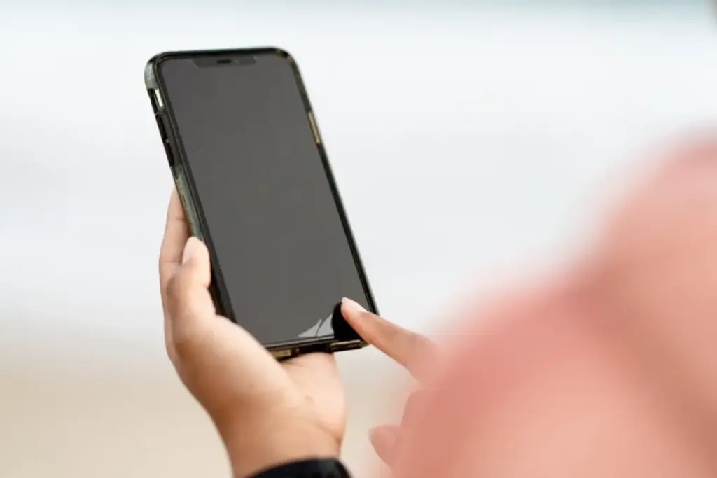 Pessoa segurando um smartphone preto enquanto toca na tela do celular com o dedo.