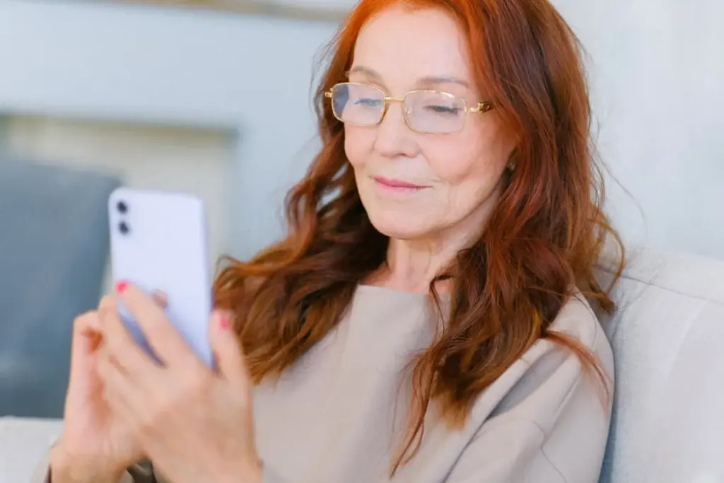 Mulher mais velha usando smartphone e olhando para a tela sentada em casa