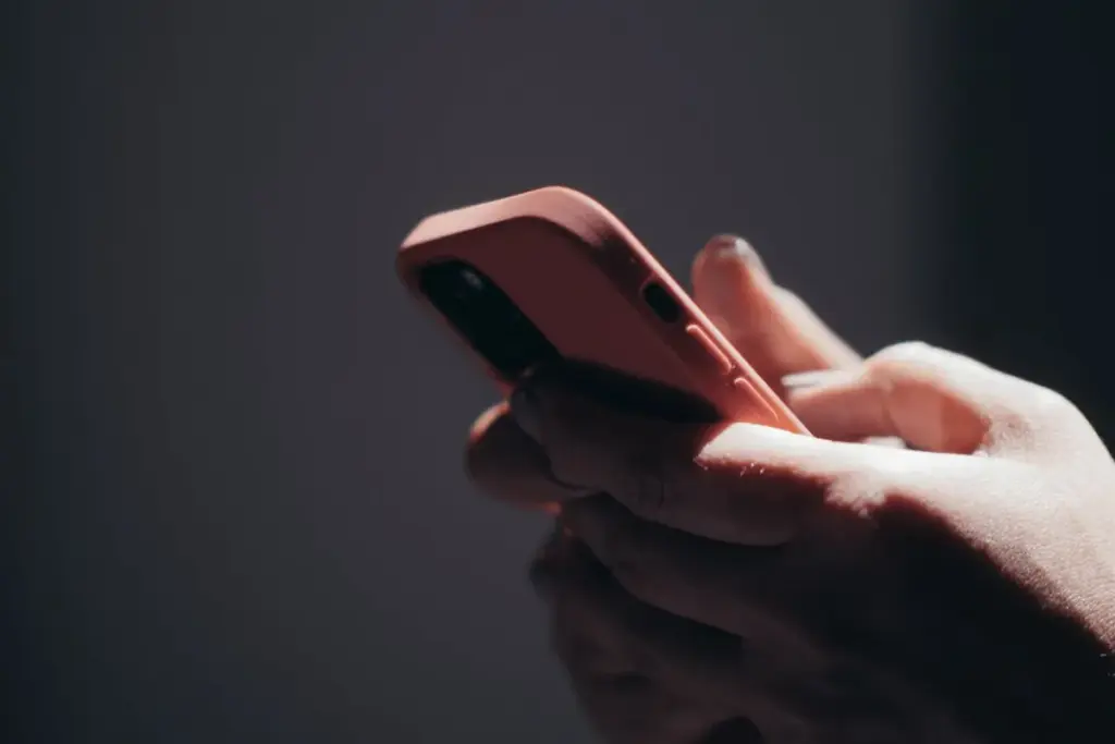 Mãos segurando smartphone enquanto uma pessoa interage com a tela em ambiente escuro