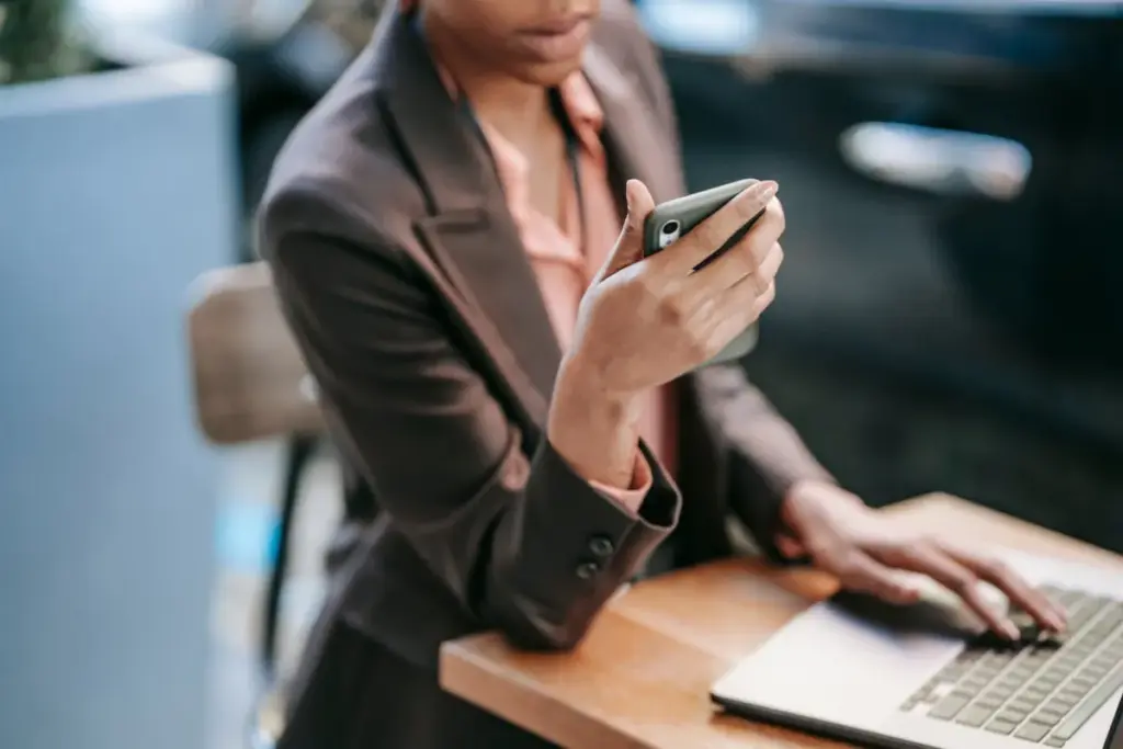 Pessoa utilizando celular enquanto trabalha no notebook em uma mesa
