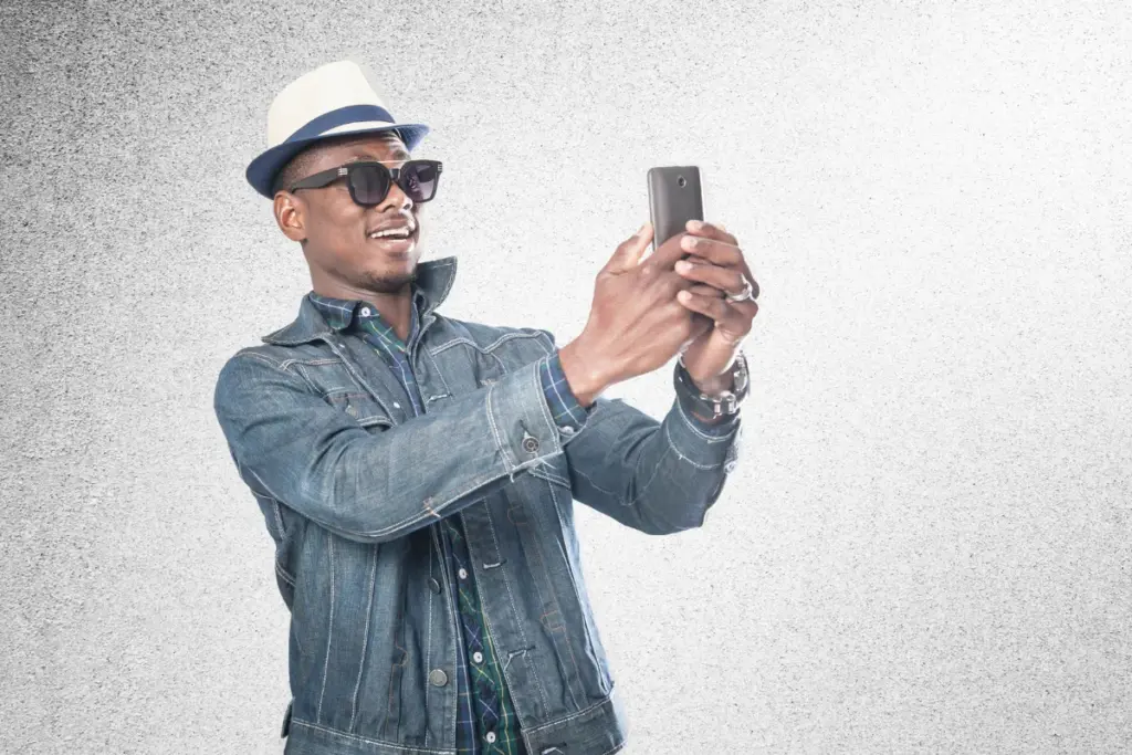 homem usando chapéu e óculos escuros tirando uma foto com o smartphone