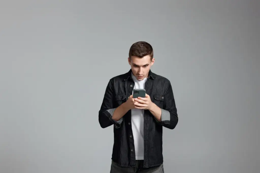 homem em pé olhando atentamente para a tela do smartphone enquanto segura o aparelho com as duas mãos