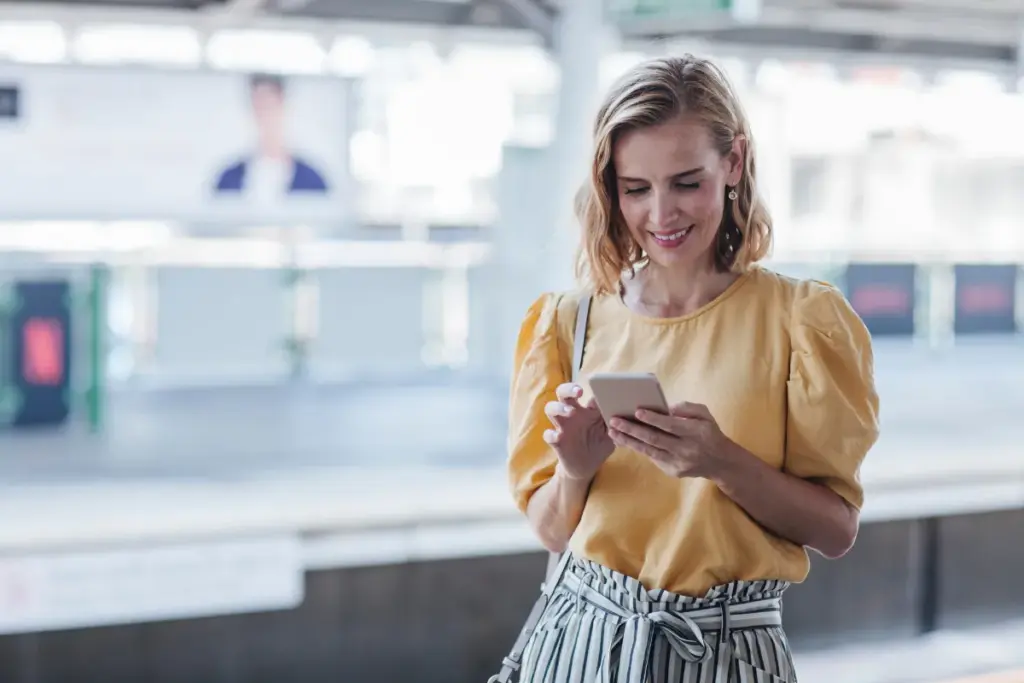 Mulher em um espaço público usando o celular enquanto olha para a tela com atenção.