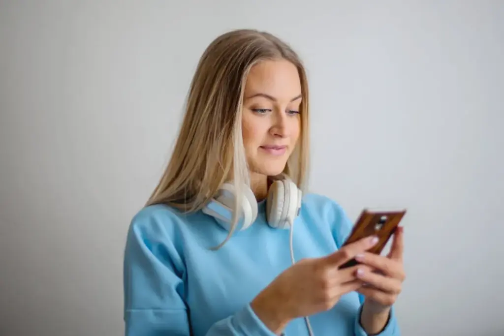 Mulher com fones no pescoço usando smartphone com as duas mãos em ambiente interno